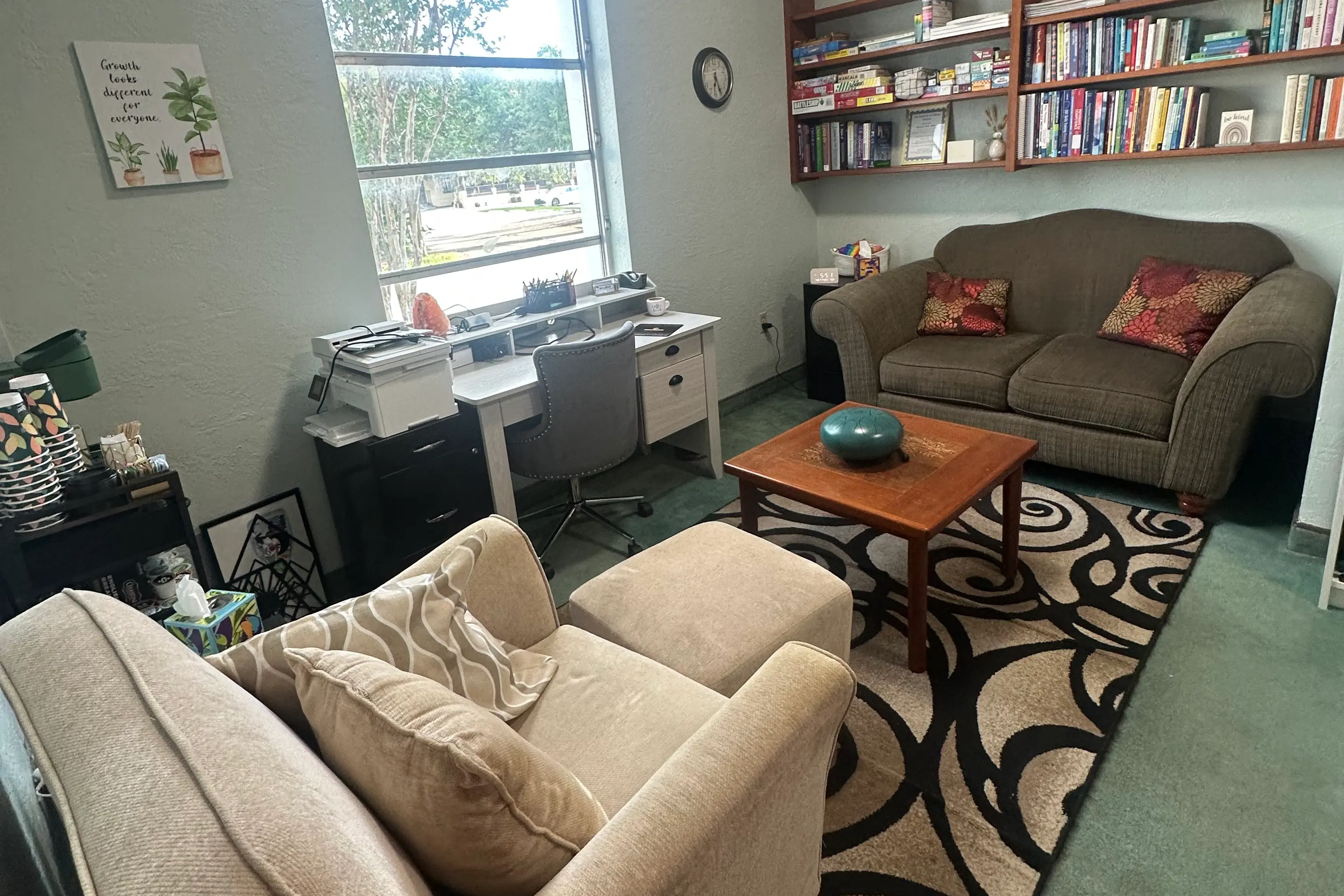 The therapy room at Replenish Counseling — a window-lit space with a sofa, armchair, coffee table, and a wall of bookshelves